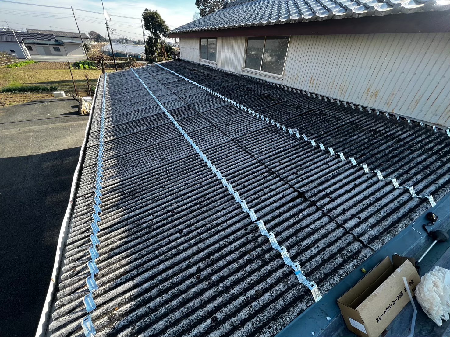 白岡市の倉庫 既存屋根の上に固定金具を並べて取り付けた工事中の様子